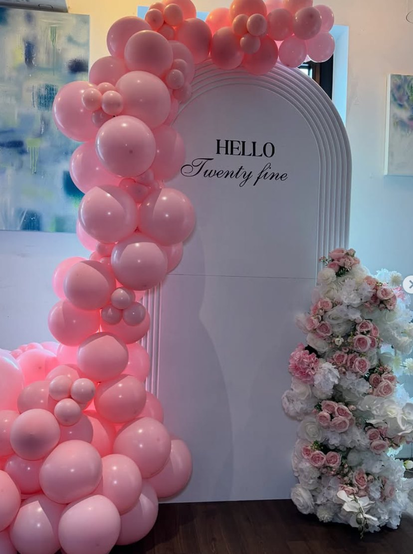 Pink balloon garland on a white arch reading Hello Twenty Fine with a floral column by TA Luxe Events