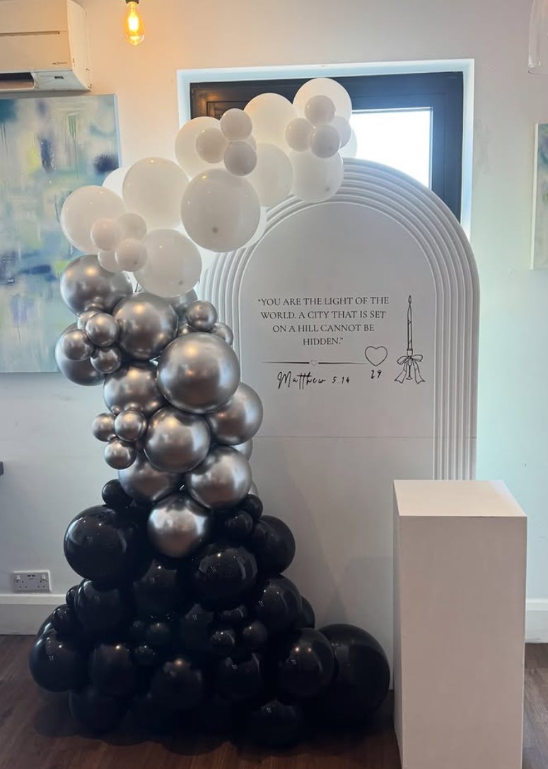 Black, silver and white balloon tower beside a white scripture arch board